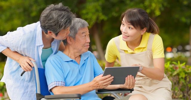 A Woman Standing Beside the Elderly Man Holding a Tablet